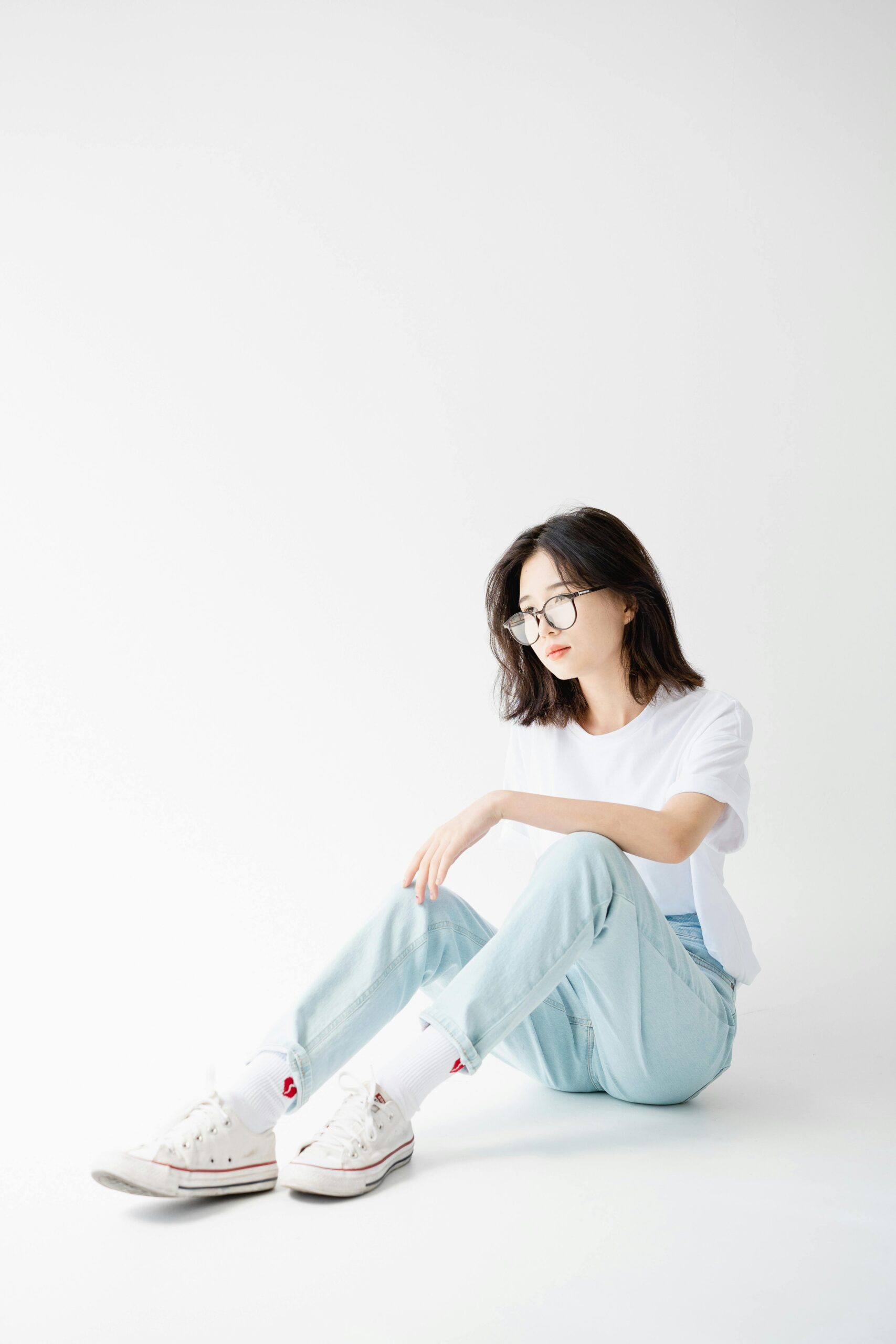 Fashionable woman with eyeglasses sitting on white background in casual style.